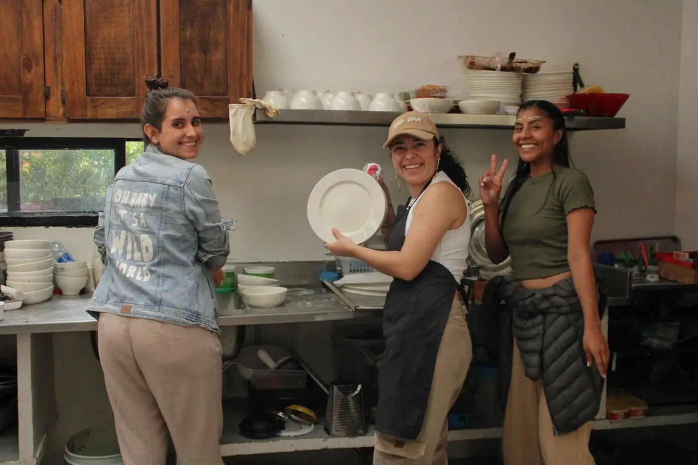 Tres personas sonriendo mientras lavan los platos después de la comida